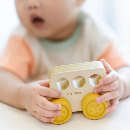 Young child playing with Plantoy yellow wooden bus toy