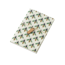 A pocket notebook with a beige cover featuring a green and yellow bee pattern and a brown closure.