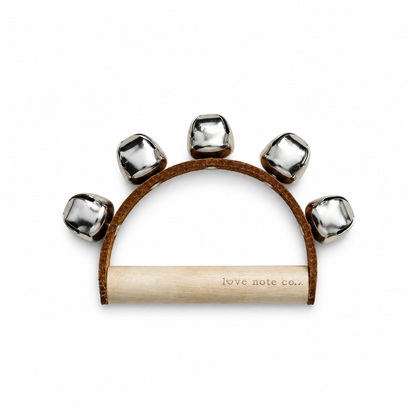 A hand-held tambourine with five silver metal bells on a brown leather arch and a light wood handle, featuring the brand name 'love note co.