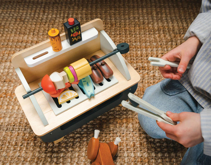 Toy barbecue set with a person holding tongs on a textured surface