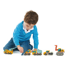 Young boy sitting on floor playing with 5 small yellow wooden construction vehicle toys