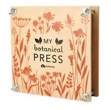 A wooden botanical flower press with metal screws at each corner, featuring a floral pattern and the text 'MY botanical PRESS' on the front.