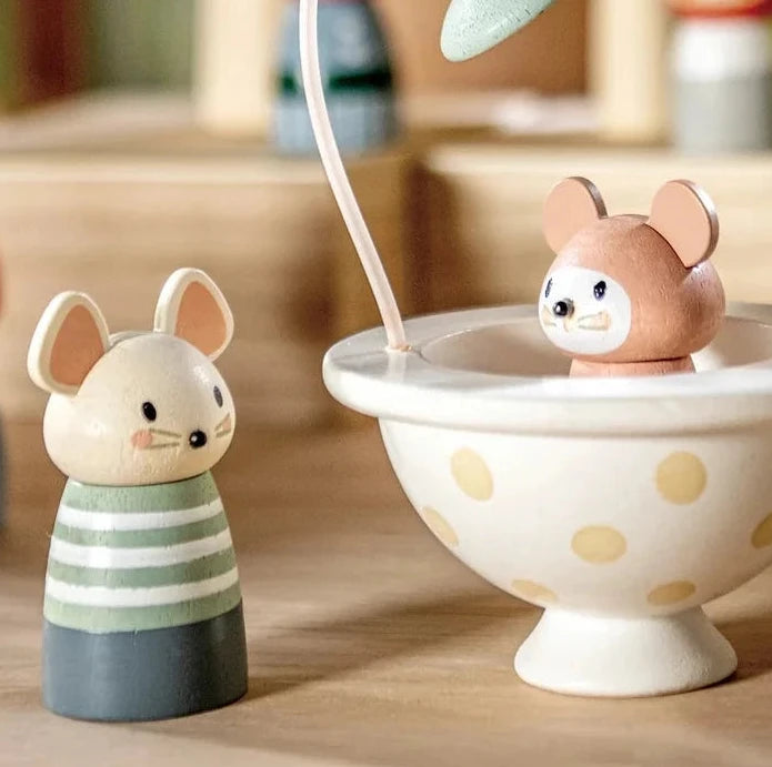 Miniature scene with figurines around a teacup and saucer on a wooden surface.