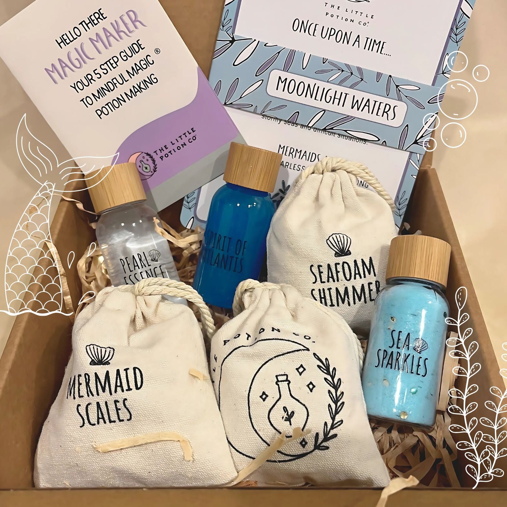 A gift box containing various items including small bottles labeled 'Mermaid Scales', 'Seafoam Whisper', and 'Sea Stars', along with recipe cards and bags decorated with mermaid-themed graphics.