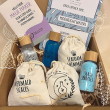 A gift box containing various items including small bottles labeled 'Mermaid Scales', 'Seafoam Whisper', and 'Sea Stars', along with recipe cards and bags decorated with mermaid-themed graphics.