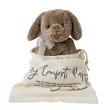 A brown plush puppy toy with a weighted body, sitting in a beige cotton travel pouch with the text 'My Comfort Puppy' printed on it.