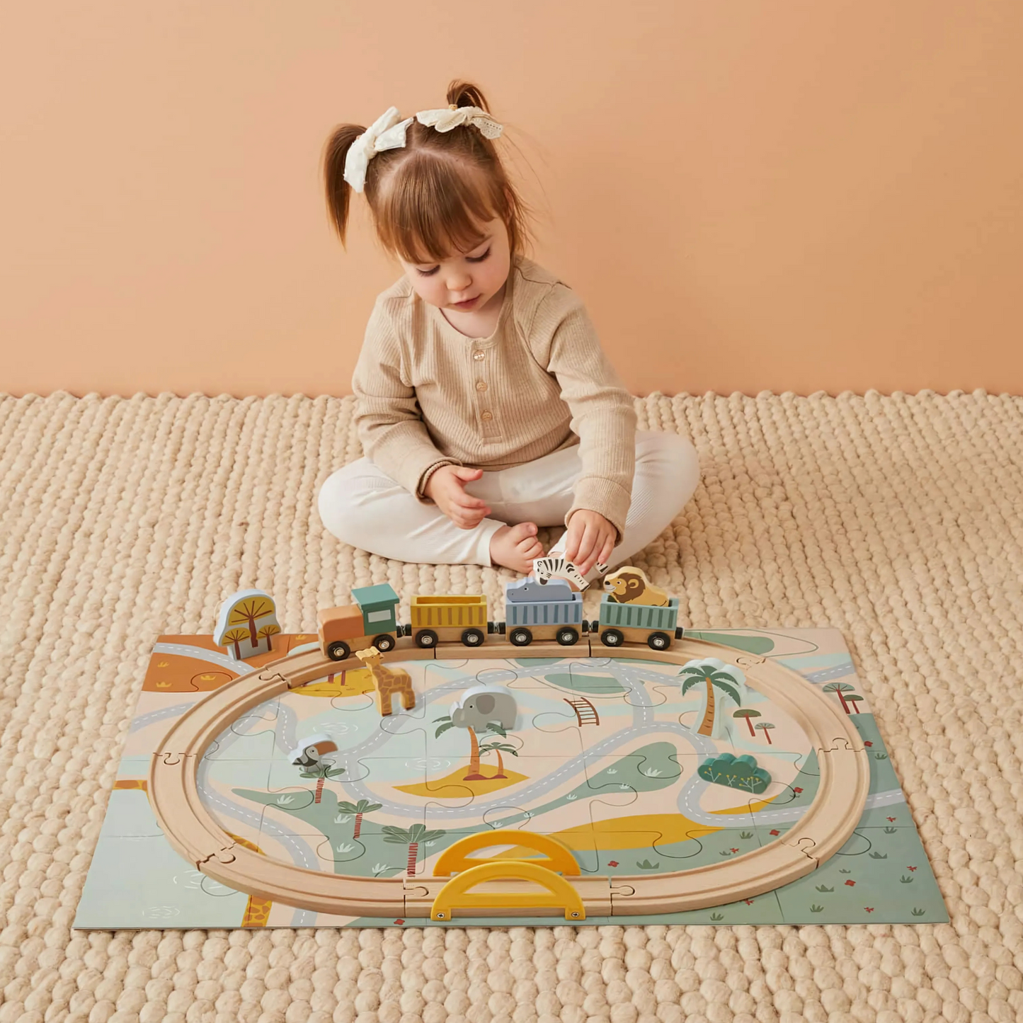 A child playing with a wooden train set featuring animal puzzle pieces on a playmat.