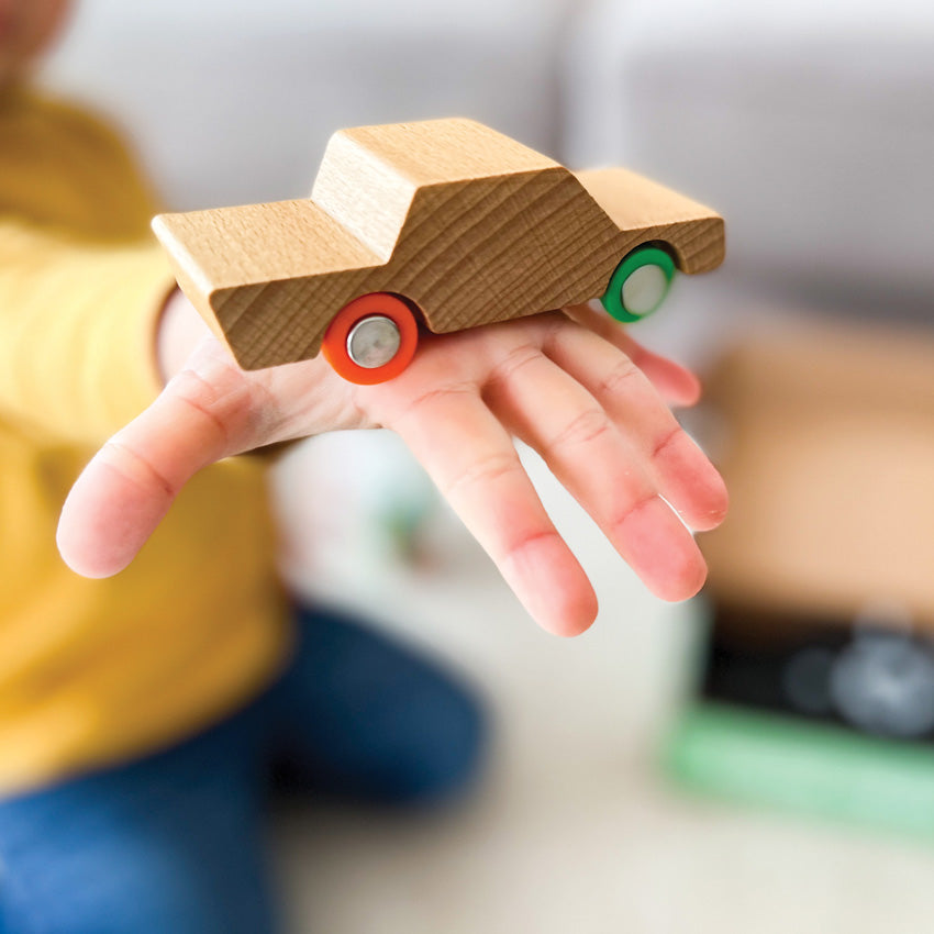 A young child’s hand holding a small wooden vehicle with a natural finish.