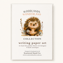 A clear acrylic sleeve encloses a printed card for a writing paper set. The card reads 'Woodlands Wonderland Collection writing paper set' with an illustration of a hedgehog and floral details, and shows the brand 'Scattered Seed Co.