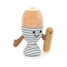 A soft toy resembling a dippy egg with smiling face in a blue and white stripe egg cup with a brown toast soldier.