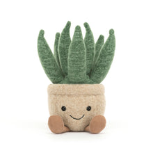 A small plush toy designed to look like an aloe vera plant with a beige pot, green leaves, and a smiling face.