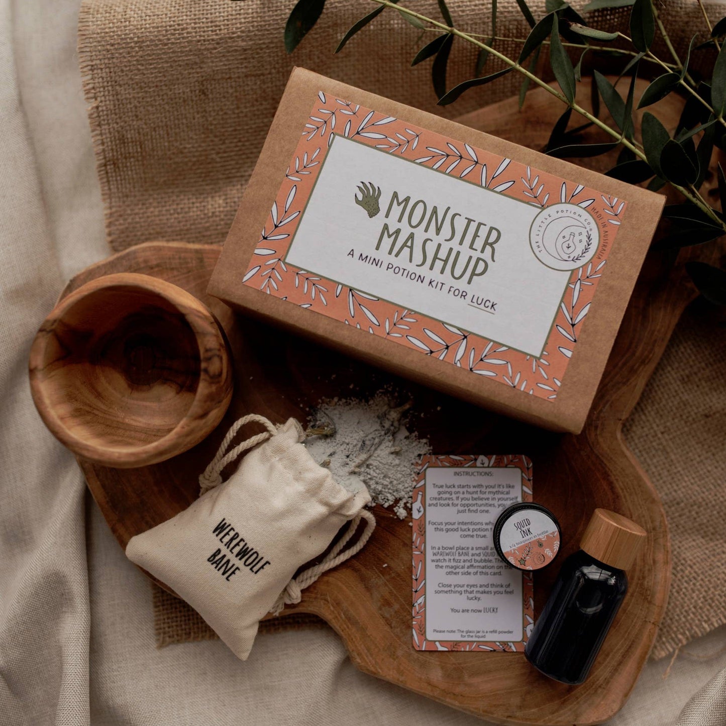 A mini potion kit for children, labeled 'Monster Mashup', with dry fizz ingredients in a cotton pouch, a sparkly liquid in a reusable PET plastic bottle, a 10ml glass jar of refill liquid powder, and a mini affirmation and spell card, all displayed on a wooden surface with a natural background.