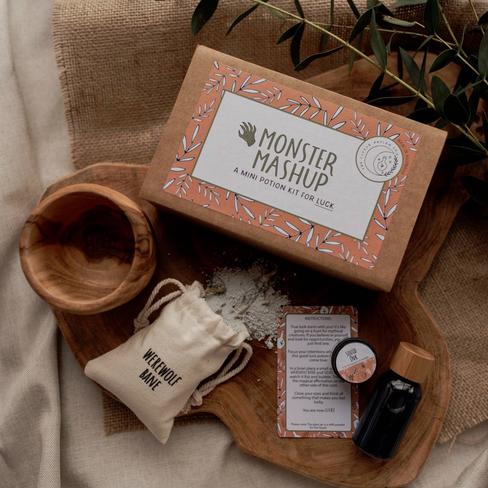 A mini potion kit for children, labeled 'Monster Mashup', with dry fizz ingredients in a cotton pouch, a sparkly liquid in a reusable PET plastic bottle, a 10ml glass jar of refill liquid powder, and a mini affirmation and spell card, all displayed on a wooden surface with a natural background.