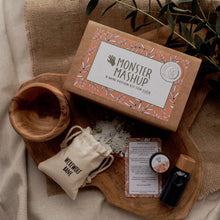 A mini potion kit for children, labeled 'Monster Mashup', with dry fizz ingredients in a cotton pouch, a sparkly liquid in a reusable PET plastic bottle, a 10ml glass jar of refill liquid powder, and a mini affirmation and spell card, all displayed on a wooden surface with a natural background.