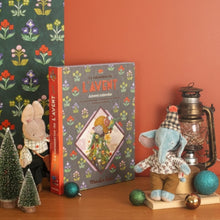 Decorative items including a book titled 'Lavent', small trees, and a teddy bear on a wooden surface with floral-patterned paper in the background.