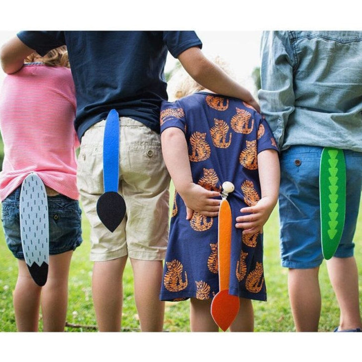 Children with colorful animal tails pinned to their backs in a grassy outdoor setting