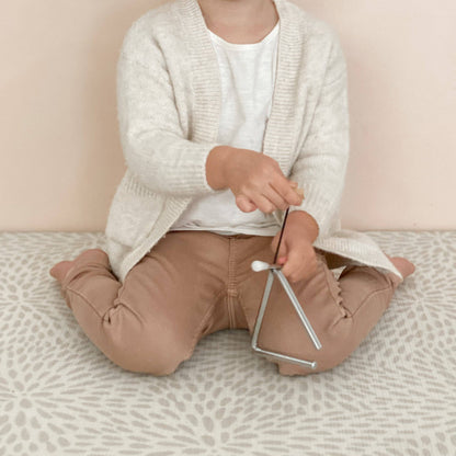 Child seated on a patterned rug playing the Love Note Co mini triangle musical toy.