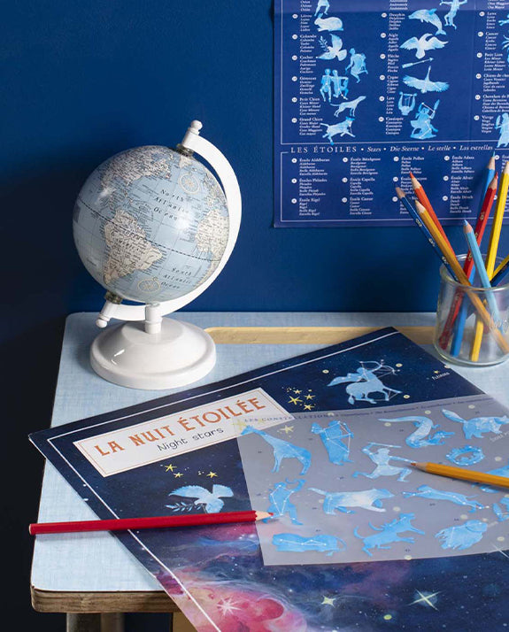 Children's educational materials on a table with a globe and star map against a blue wall.