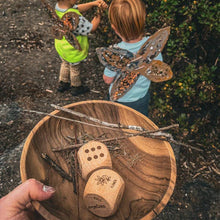Wooden bowl with carved dice and natural elements, children playing in the background