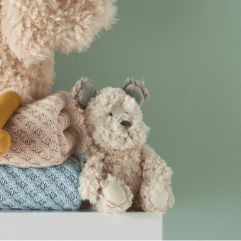 Fluffy teddy bear with a knitted blanket on a light green background
