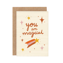 A greeting card with the text 'you are magical' surrounded by sparkles and shooting stars illustrations. The card is accompanied by a brown Kraft envelope.