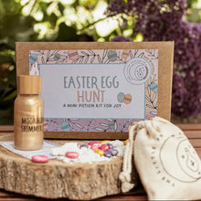An Easter Egg Hunt Potion Kit displayed outdoors, including a cotton bag, a bottle with a liquid ingredient, a glass jar with powder, and a spell & affirmation card.