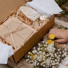 A hand-crafted wooden flower press kit displayed alongside pressed flowers, with the kit components arranged neatly, including cards, envelopes, a wooden keyring, and a paintbrush.
