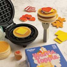 Waffle Topple game set with waffle maker, toy food items, and game box on a marble surface.