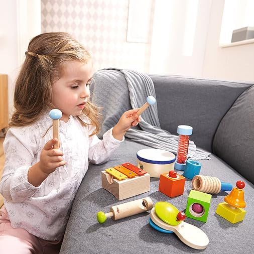A child playing with a variety of colorful musical toys on a couch, including a maraca, drum, and other small percussion instruments.