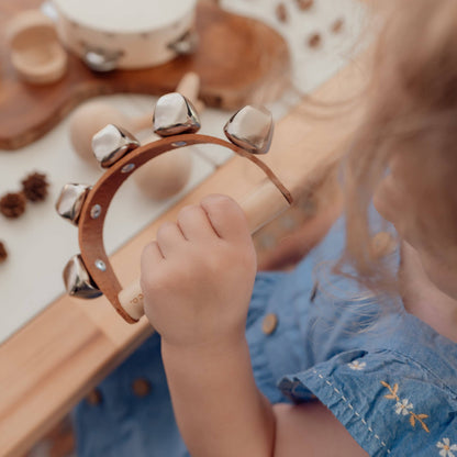 Child holding the Love Note Co handbells musical toy beside a wooden activity table.