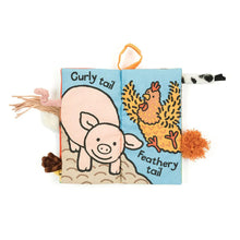 A padded fabric book with a pig and chicken printed on the displayed page. The words Curly Tail Feathery tail are also printed on the page. Various tactile animal tails are sticking out both sides of the book. 