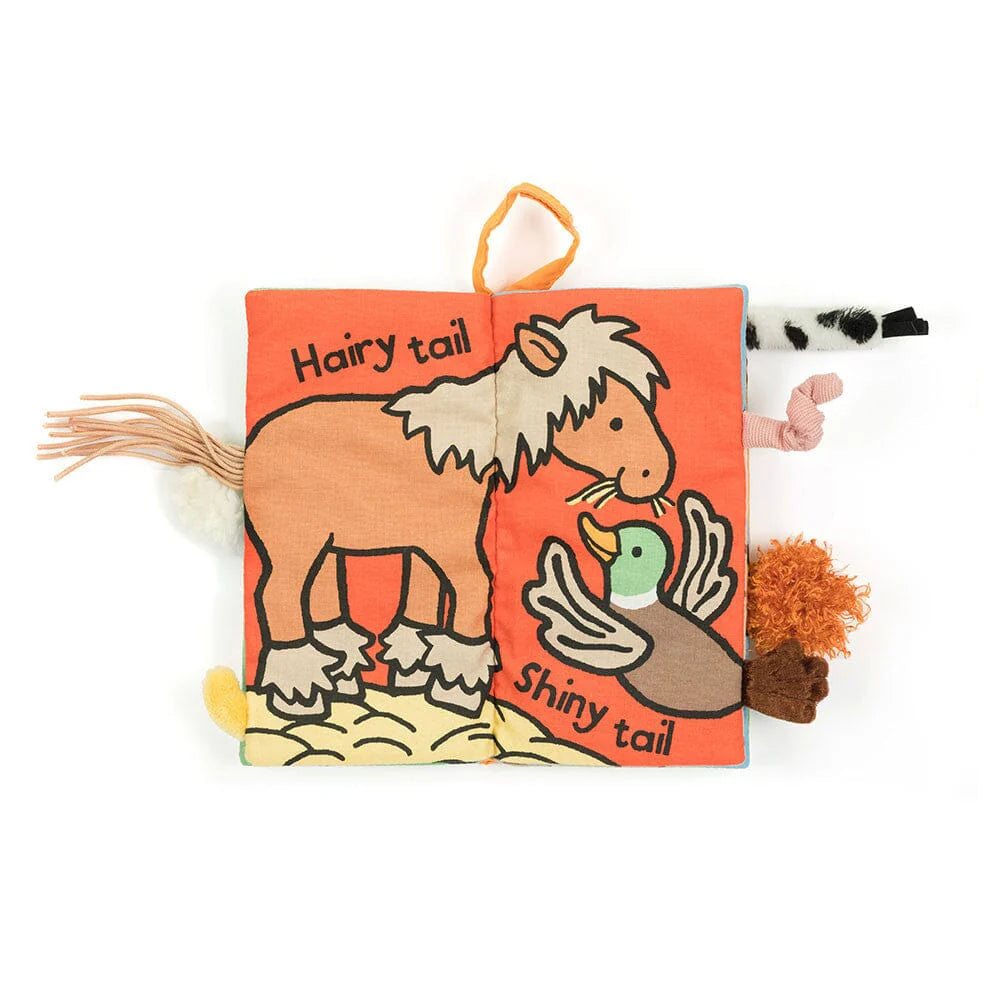 A padded fabric book with a horse and duck printed on the displayed page. The words Hairy Tail Shiny tail are also printed on the page. Various tactile animal tails are sticking out both sides of the book. 