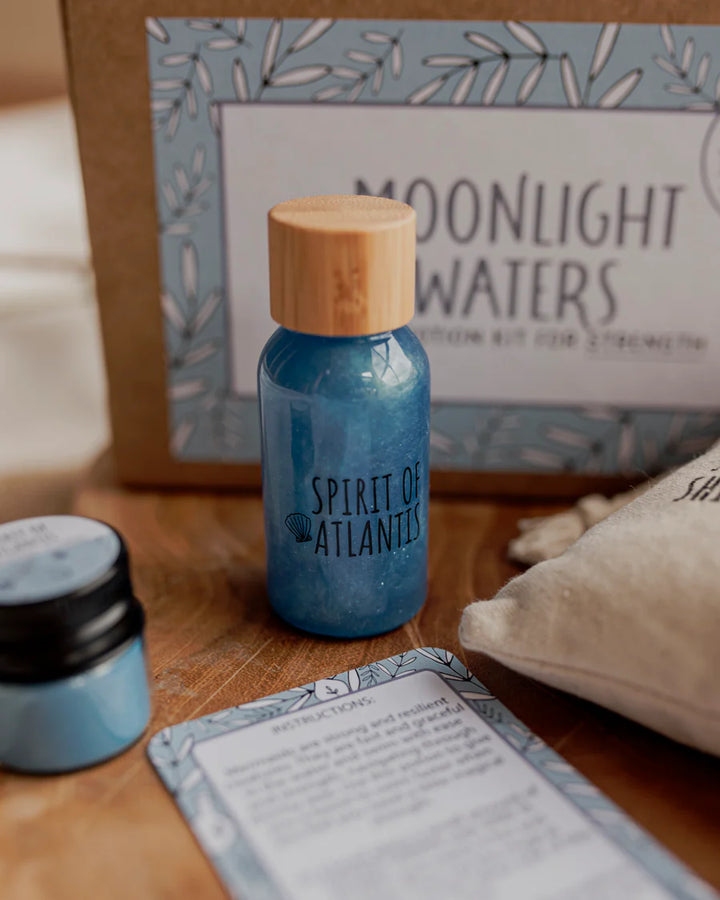 Blue bottle labeled 'Spirit of Atlantis' with a wooden cap on a wooden surface, with 'Moonlight Waters' packaging in the background.