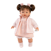 A 33cm crying doll with a pink dress, white vinyl limbs, and a fringe hairstyle. It is holding a pacifier and wearing a pink jacket and white bloomers.