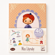 A boxed sticker activity product labeled 'Miss Lilyruby' with '40 stickers removable' shown on the front. The packaging features a pastel illustration of a girl with red hair and a red polka-dot hat on an orange patterned background, with sample sticker sheets and clothing stickers visible below.