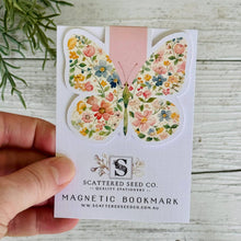 A floral patterned magnetic bookmark with a butterfly design, displayed on a white background with a wooden texture.