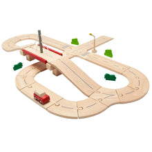 Wooden toy road system set including tracks, a bridge, a car, a street light, and bushes, all in a natural wood color palette.