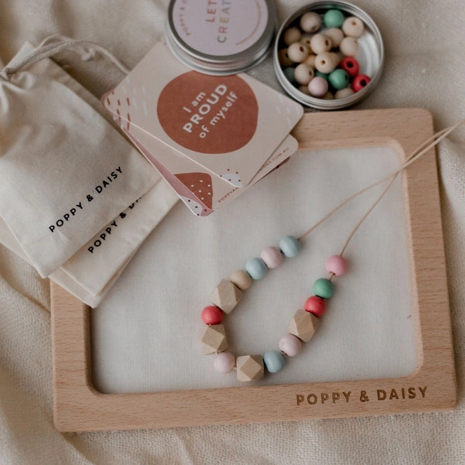 Craft kit contents displayed, including wooden beads, cotton cord, beading board, glue, paintbrush, and gift bags.