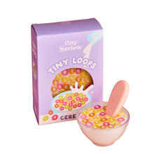 Bowl of dolls pretend colorful cereal with a spoon next to a Tiny Harlow cereal box on a white background