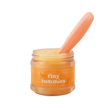 Jar of 'tiny tummies' banana custard with a pink spoon on a white background