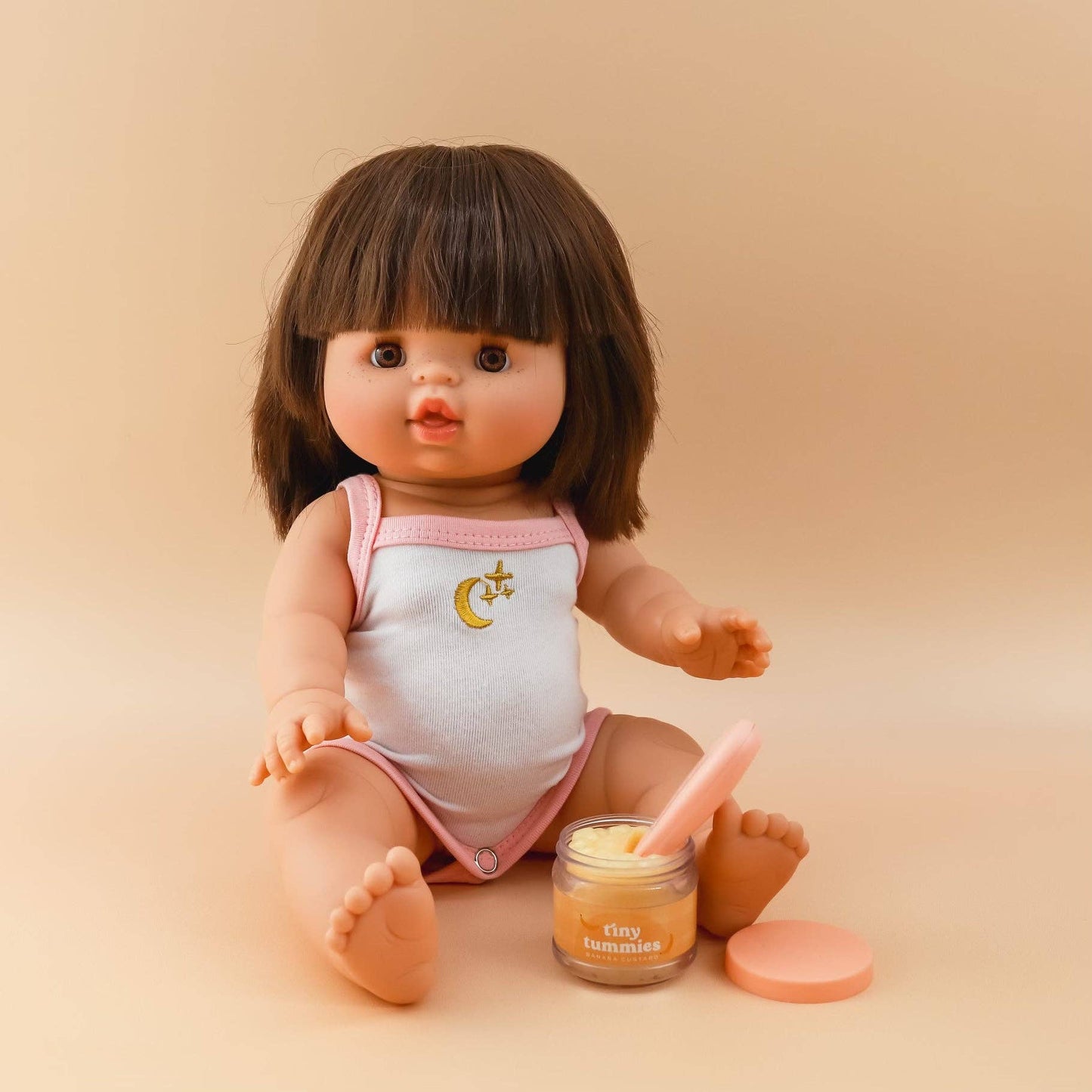 Baby doll with a jar of pretend play baby food on cream on a beige background