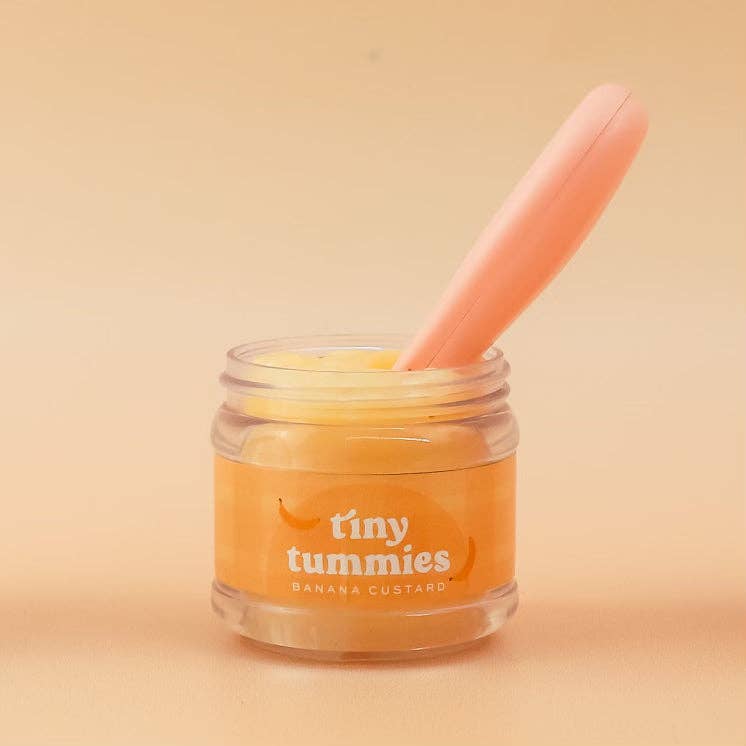 Jar of 'tiny tummies'prretend play  banana custard with a pink spoon on a beige background