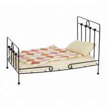Small metal doll bed with a quilt and pillow on a white background