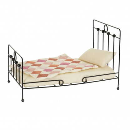Small metal doll bed with a quilt and pillow on a white background