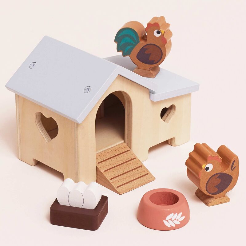 Wooden toy chicken coop with rooster and hen figures on a light pink background