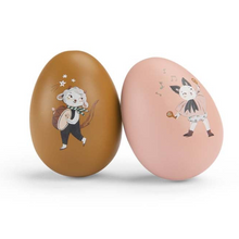 Two wooden musical eggs with illustrations of musical instruments and characters on a pink background.