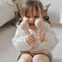 Child playing with Love Note Co wooden maracas in a warm neutral playroom.