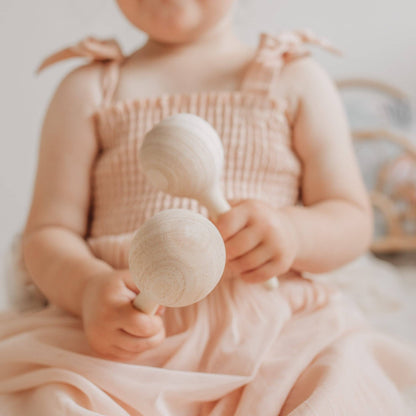 Child in a pink dress holding a pair of Love Note Co wooden maracas.