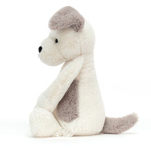 A plush toy resembling a terrier dog with a cream body, gray patches on the head and back, and a white face.