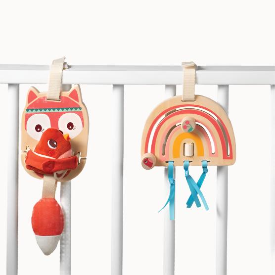 Fox and rainbow baby activity toys made of wood and other assorted materials, attached to white wooden bars resembling the side of a babies cot.